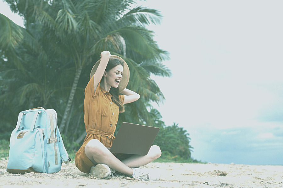 Image of woman with hat laughing at computer on a beach